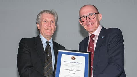 Anthony Buttler being awarded a certificate for the Fellow of the Royal Aeronautical Society. The two men are wearing suits and holding the certificate in the frame. They are smiling at the camera.